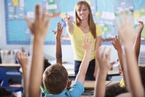 The role of a teaching assistant. Children with their hands up in a classroom