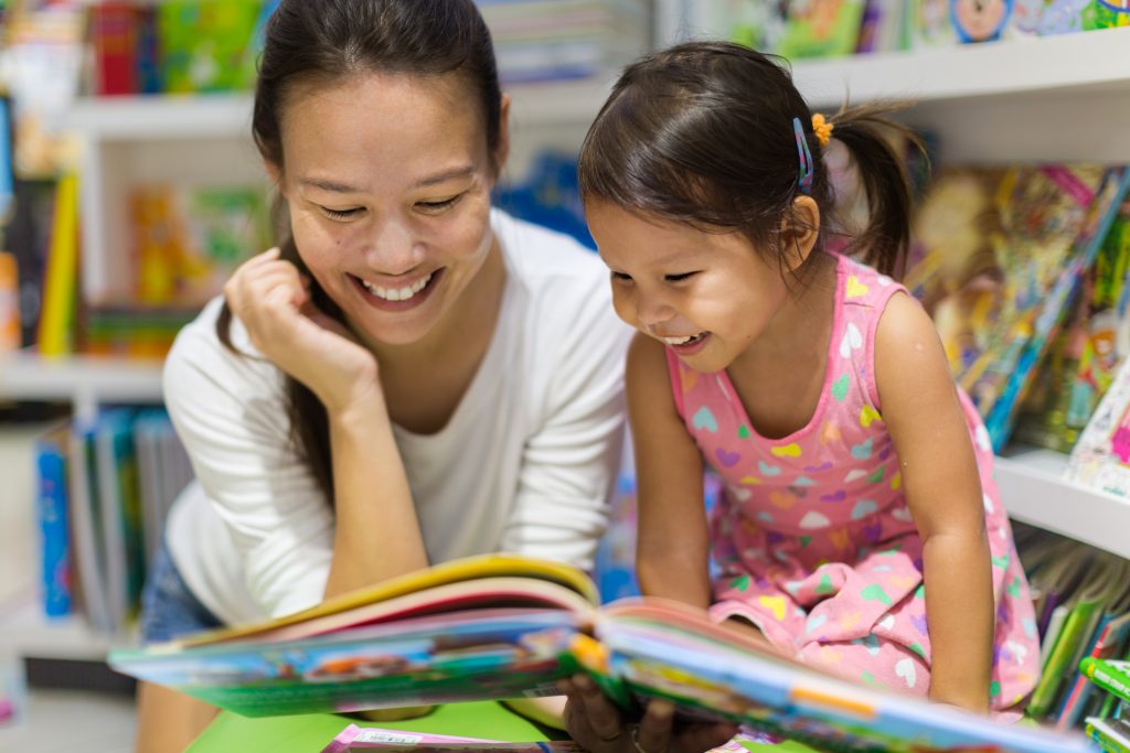 Teacher and child in library reading a book together.