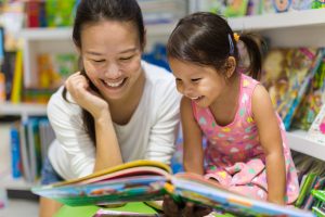 Teacher and child in library reading a book together.