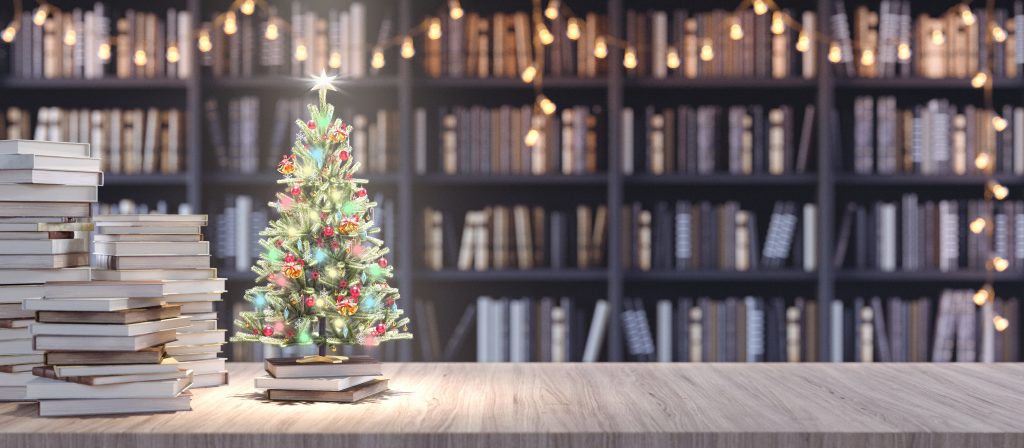 Library desk with Christmas lights and tree with books in the background.